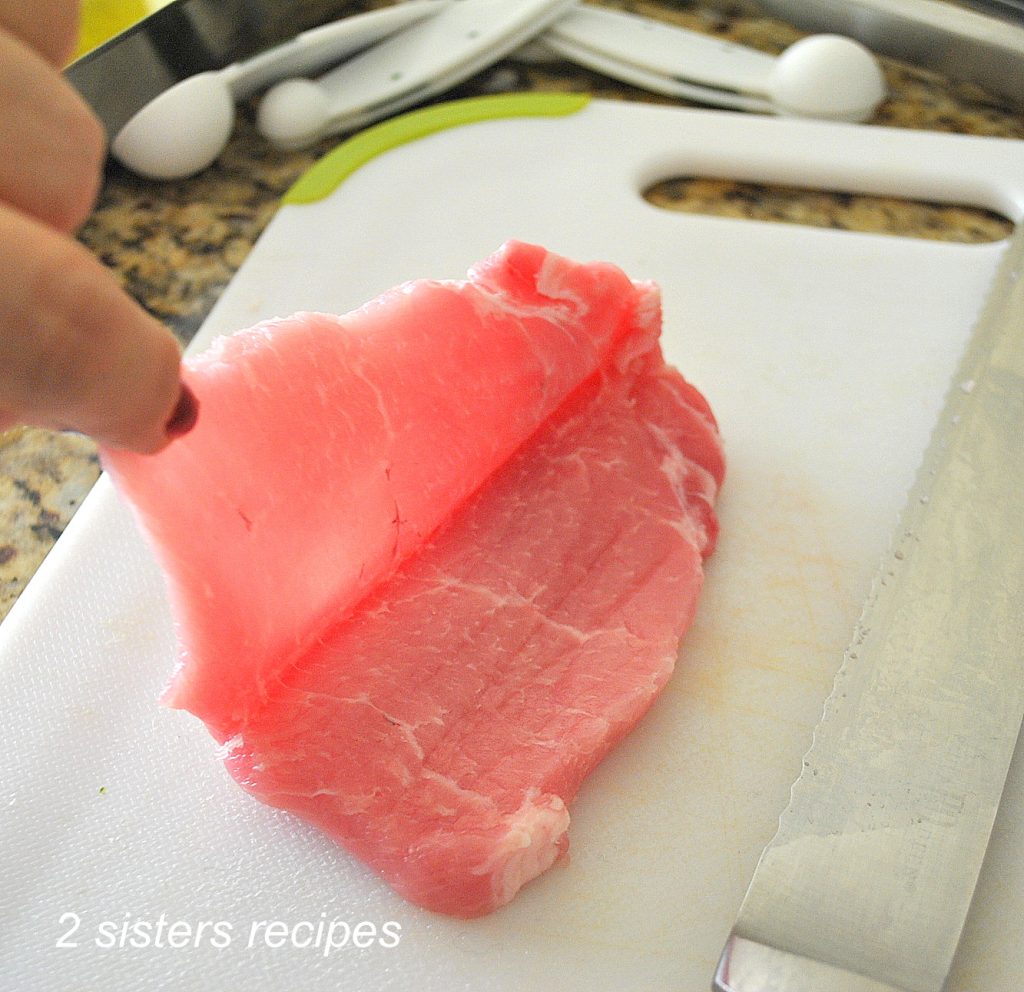 One pork chop is butterflied on a white board.  by 2sistersrecipes.com