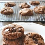 A bunch of dark chocolate chip cookies set on a white plate.
