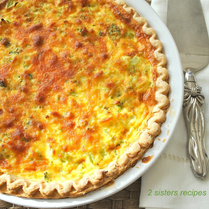 A pie plate with a quiche baked in a crust with a serving knife on the side.