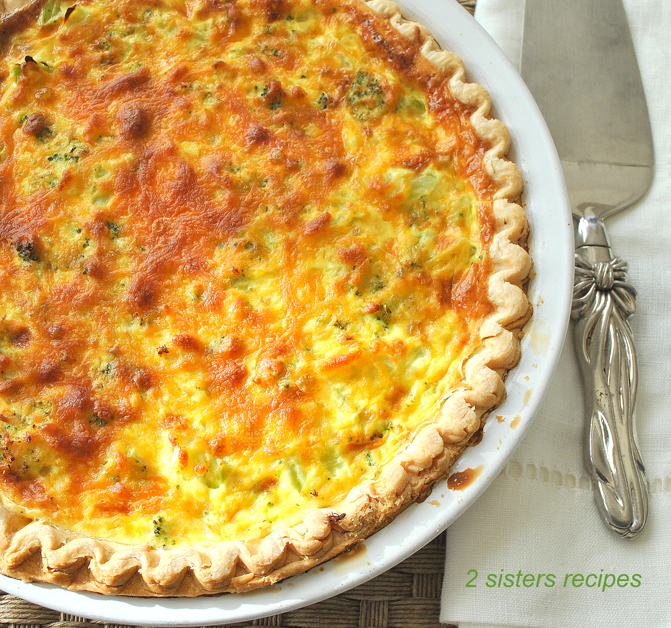 A pie plate with a quiche baked in a crust with a serving knife on the side.