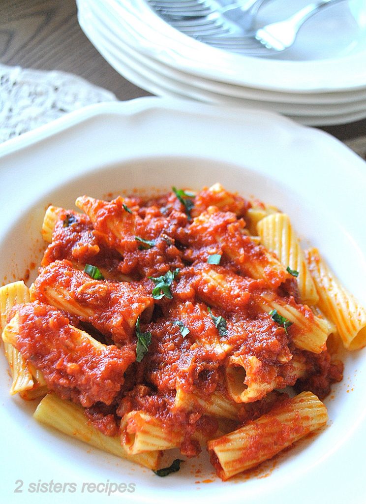 A white pasta dish filled with rigatoni pasta with tomato sauce.