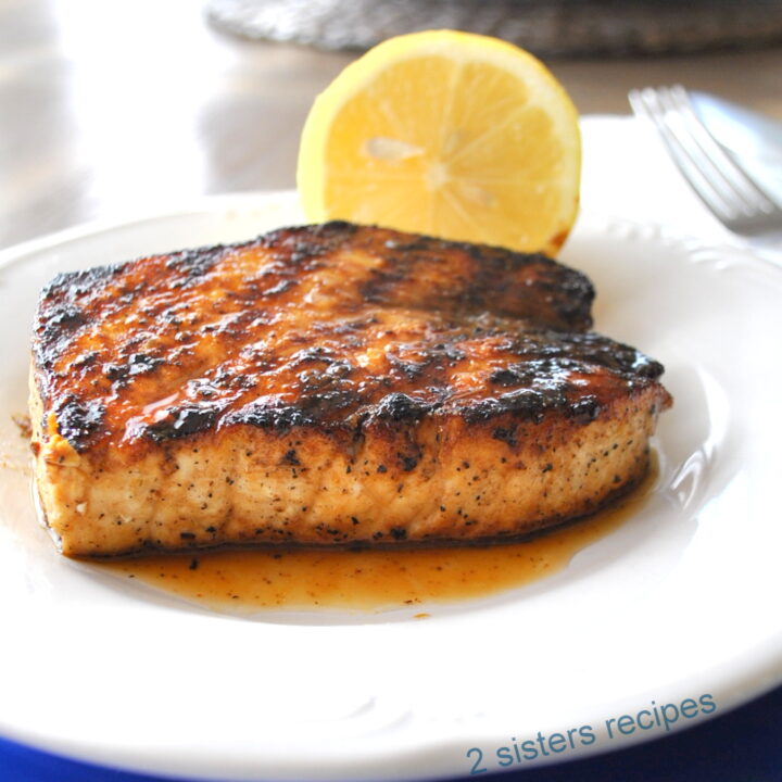 A grilled swordfish served on a white plate with a lemon on the side.