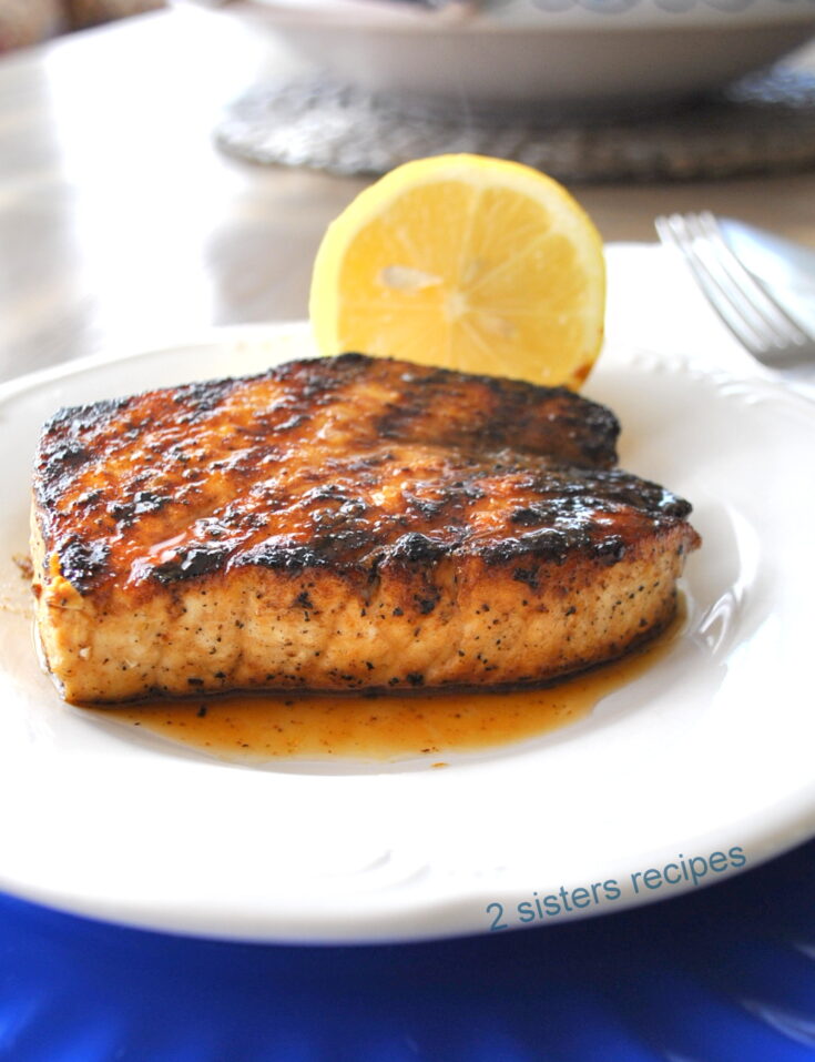 A grilled swordfish served on a white plate with a lemon on the side.