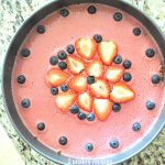 A springform cake pan with a pink colored top and blueberries with sliced strawberries on top. by 2sisterserecipes.com