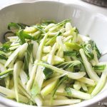 A white salad bowl filled with thinly sliced bok choy and green apples