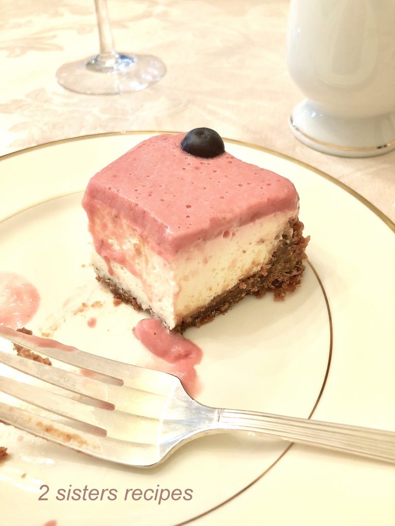  A slice of Lemon Raspberry Panna Cotta Cheesecake on a white plate. by 2sistersrecipes.com