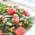 a white plate filled with arugula lettuce, cubes of watermelon and granola on top.