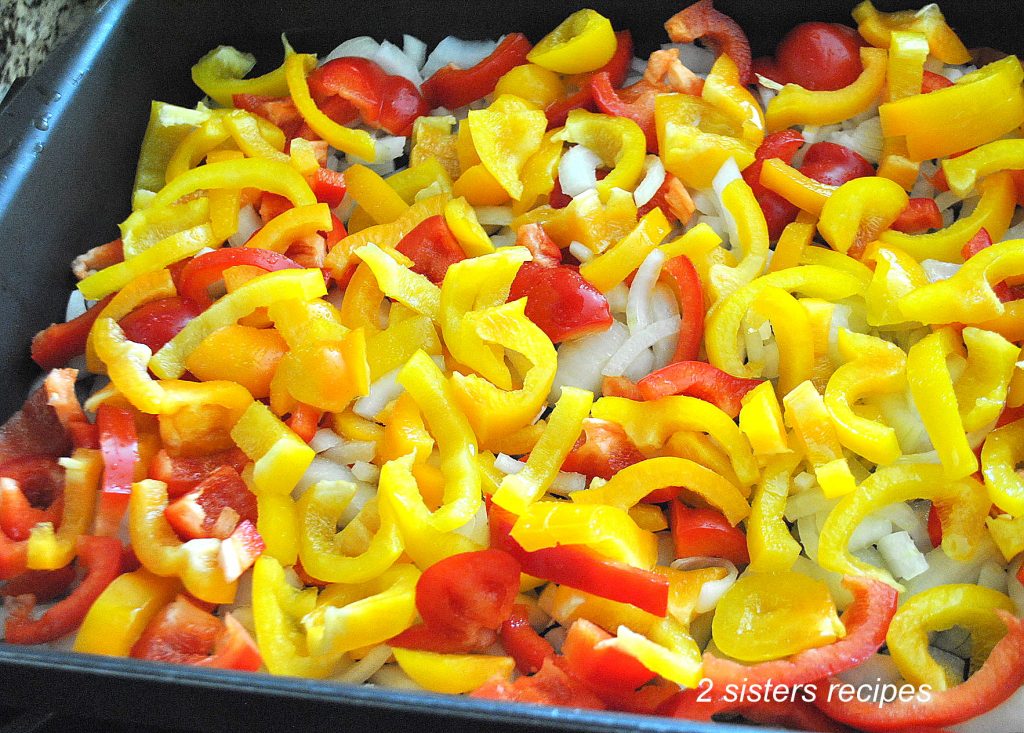 A large baking pan loaded with chopped red and yellow peppers, and onions.