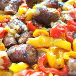 A white baking dish filled with baked yellow and red peppers and cut sausage links.