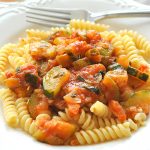 In a white pasta bowl, curly "rotini" pasta is served with a zucchini tomato sauce on top.