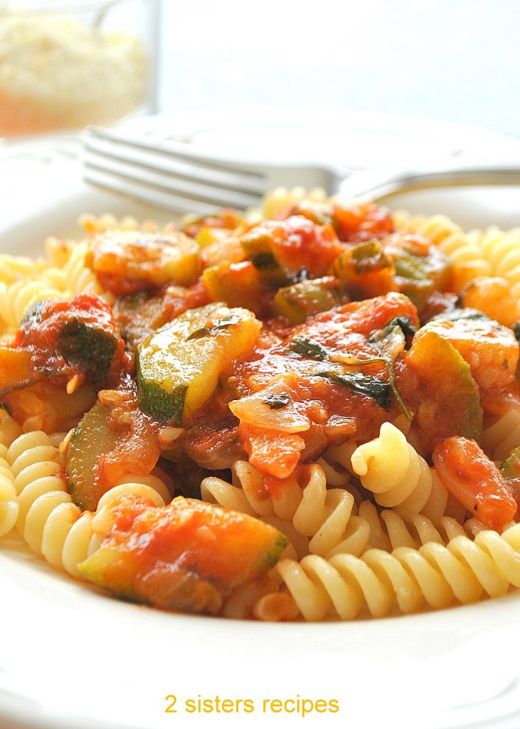 A white plate filled with curly pasta topped with zucchini and marinara sauce.