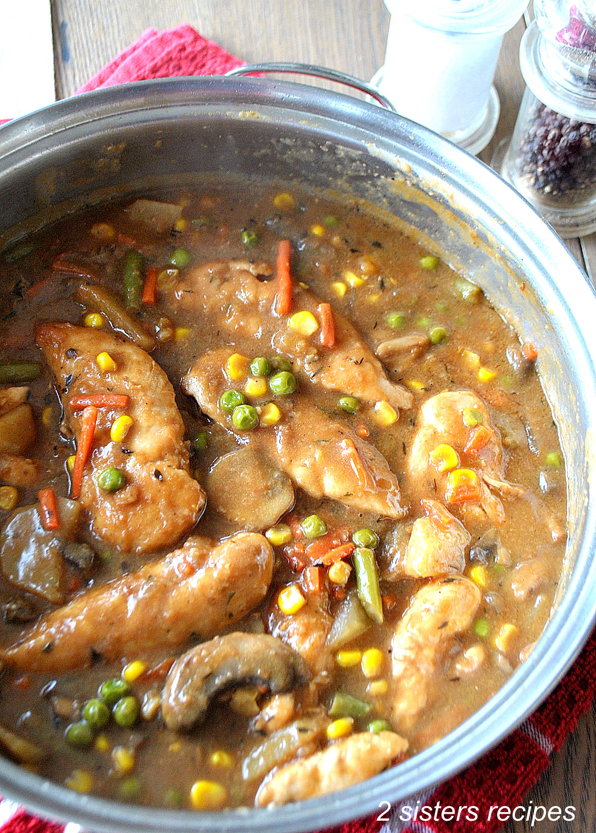 A large skillet loaded with cooked chicken tenders, vegetables and brown gravy.