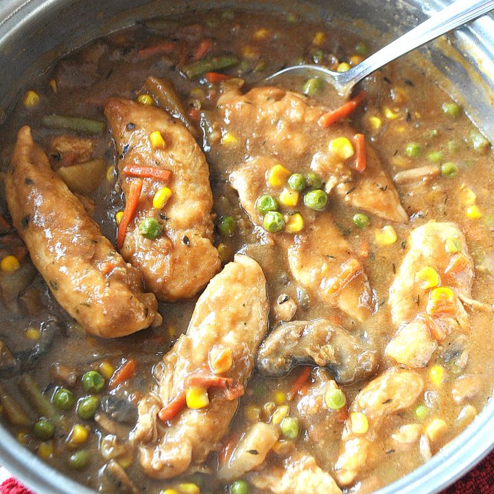 A large skillet loaded with pieces of chicken tenders and vegetables in a brown gravy.,