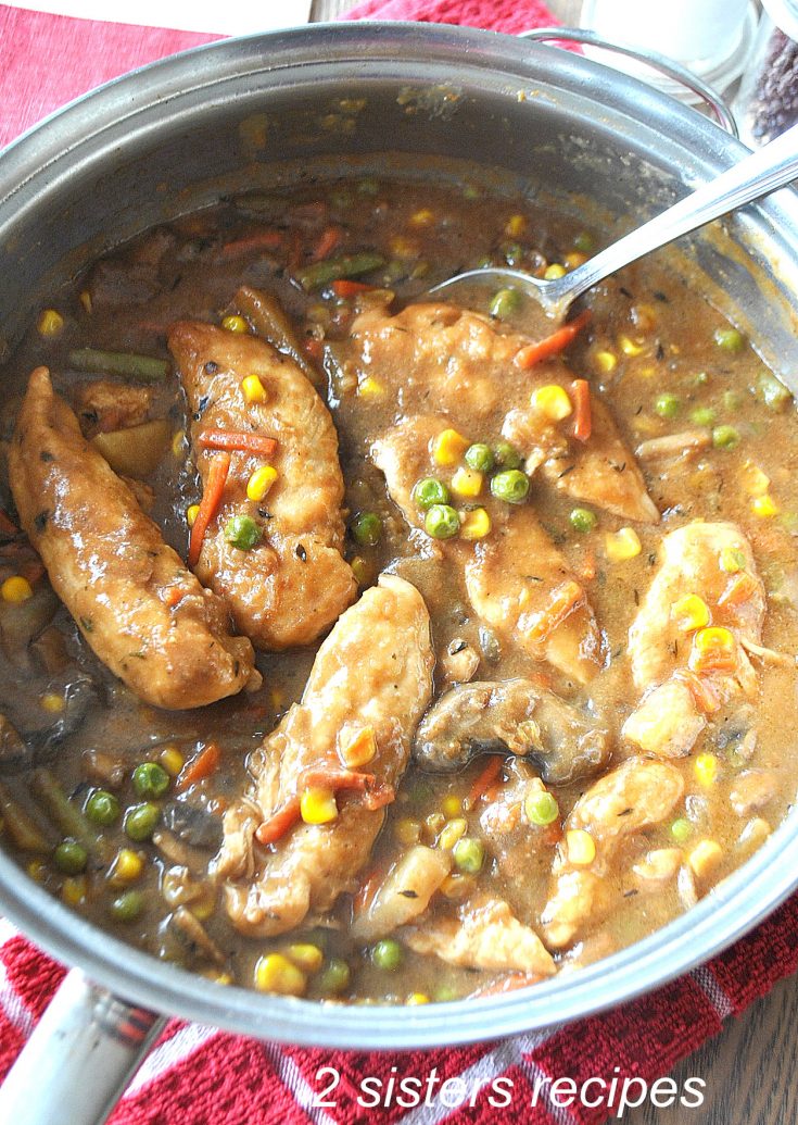 A large skillet loaded with pieces of chicken tenders and vegetables in a brown gravy.,