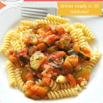 A white dish filled with fusilli pasta topped with zucchini tomato sauce.
