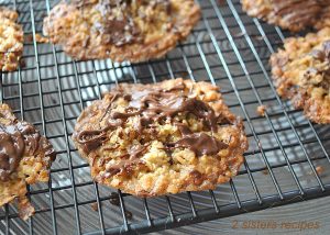Freshly baked thin cookies with melted chocolate drizzled on top cooling on a wire rack.