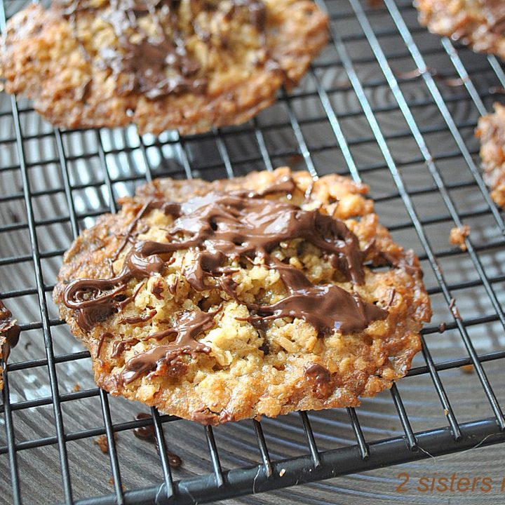 Freshly baked thin cookies with melted chocolate drizzled on top cooling on a wire rack.