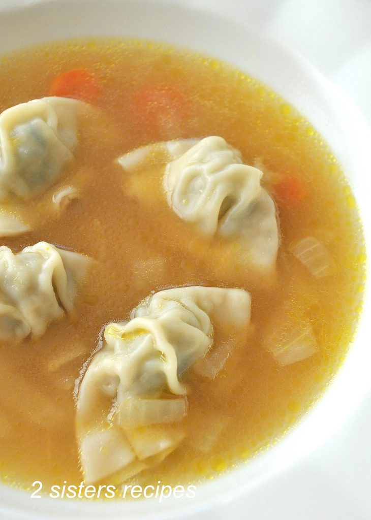 A white bowl of chicken broth with mini wontons in it.