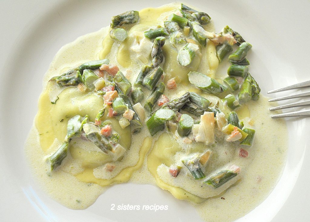 A white plate with 3 or 4 round ravioli with a cream asparagus sauce.
