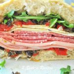An open Italian Muffuletta Sandwich filled with layers of cured meats, cheeses, roasted red peppers and arugula leaves.