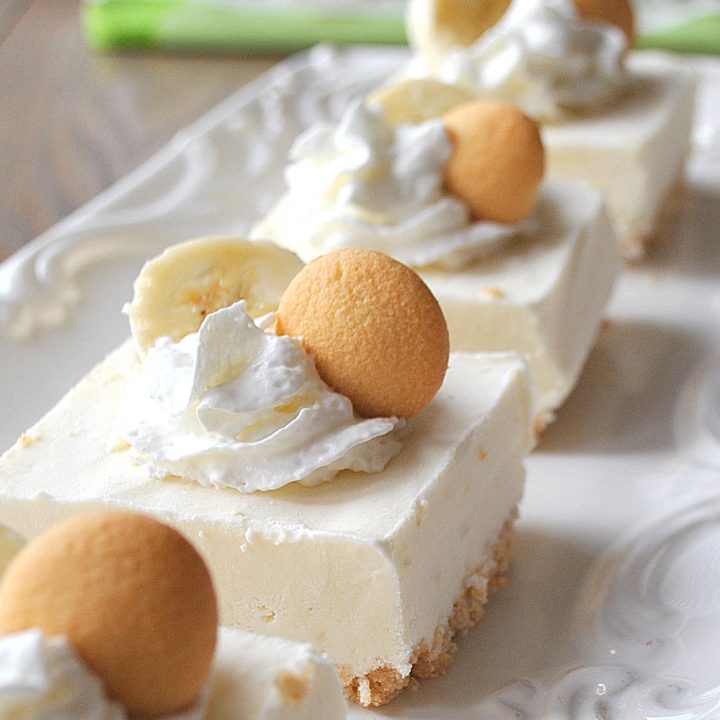 A white platter filled with banana pudding bars topped with whipped cream, a slice of banana, and a cookie.