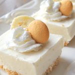 A white platter with servings of white frozen bars topped with whipped cream, a slice of banana and a Nilla cookie.