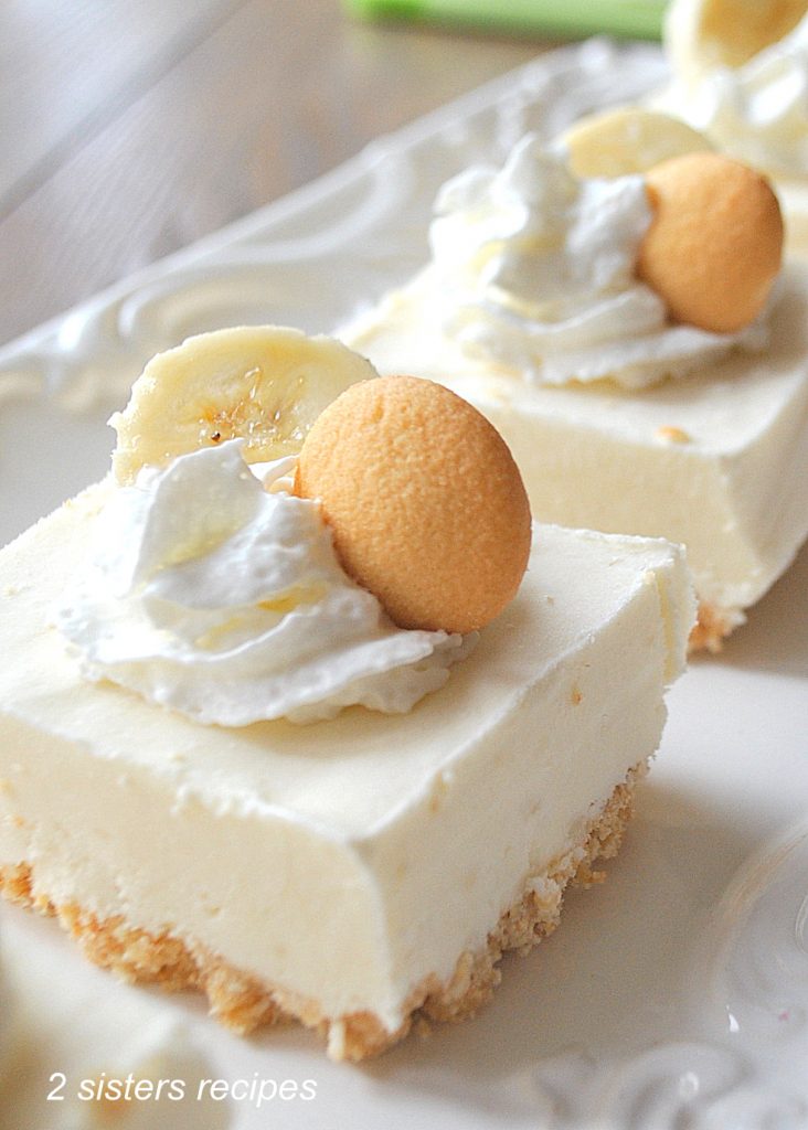 A white platter with servings of white frozen bars topped with whipped cream, a slice of banana and a Nilla cookie.