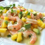 A white platter filled with a shrimp salad, loaded with chopped mango and avocado and cilantro.