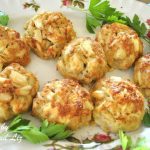 Crab Cake are served on a white platter with parsley scattered around them as garnish.