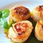 Seared Sea Scallops Over Pesto Sauce is served on a white dinner plate.