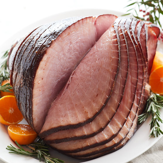 A sliced Spiral Ham with oranges on the side served on a white plate. 