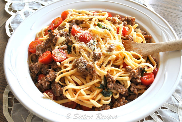 Tagliatelle pasta is tosses with cherry tomatoes and ground cooked sausages ragu served in a white round bowl.