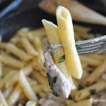 A forkful of penne pasta with a strip of veal over a large skillet on stove top.