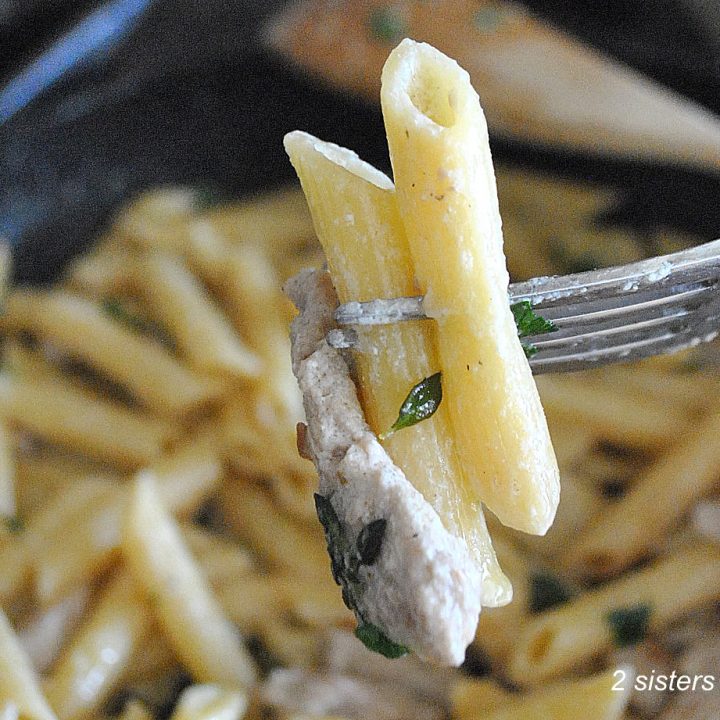 A forkful of penne pasta with a strip of veal over a large skillet on stove top.