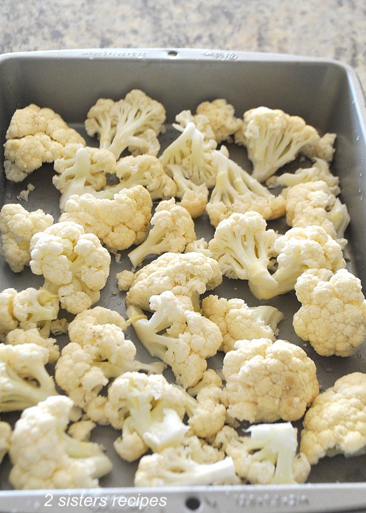 Raw cauliflower florets in a baking pan by 2sistersrecipes.com 