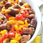 A white oval platter filled with baked sausage links and red and yellow peppers.