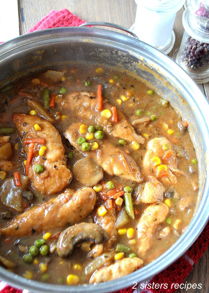 A large skillet filled with chicken tenders, and veggies smothered in a brown gravy. 