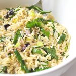 A large bowl with serving spoon of orzo and spinach salad.