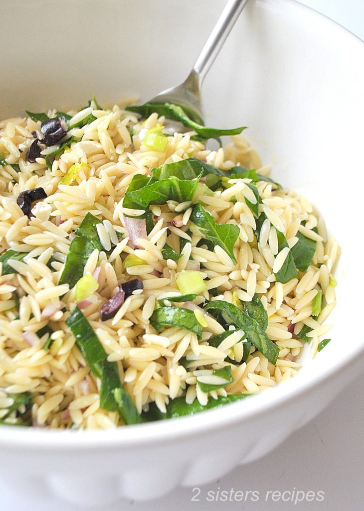 A large bowl with serving spoon of orzo and spinach salad.