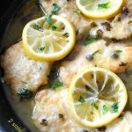 Chicken Piccata with lemon slices on top in a black skillet.