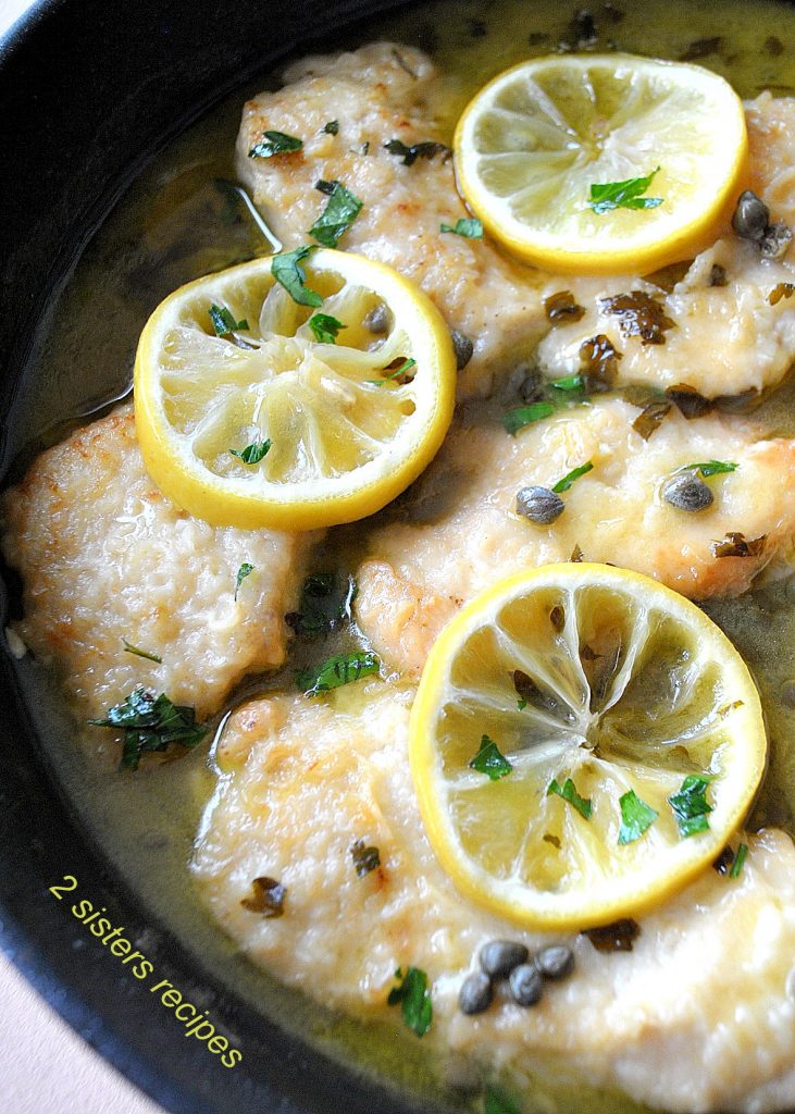 Chicken Piccata with lemon slices on top in a black skillet. by 2sistersrecipes.com