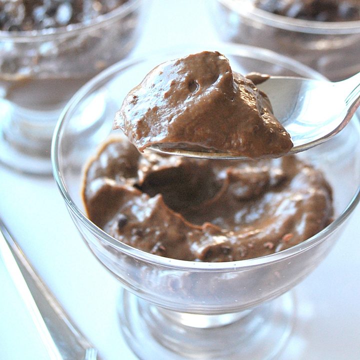 Three desserts glasses filled with chocolate pudding and a spoonful of chocolate pudding.