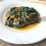 A white plate filled with a serving of sautéed spinach with two bread sticks on the side.