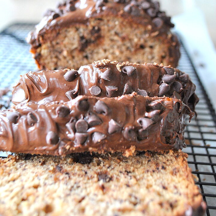 A banana bread with chocolate frosting and chocolate chips sliced on a wire rack.