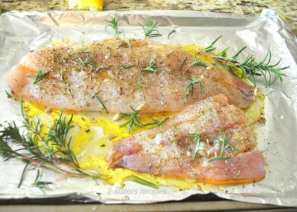 Raw red snapper filets with fresh herbs on foil wrap baking sheet. by 2sistersrecipes.com
