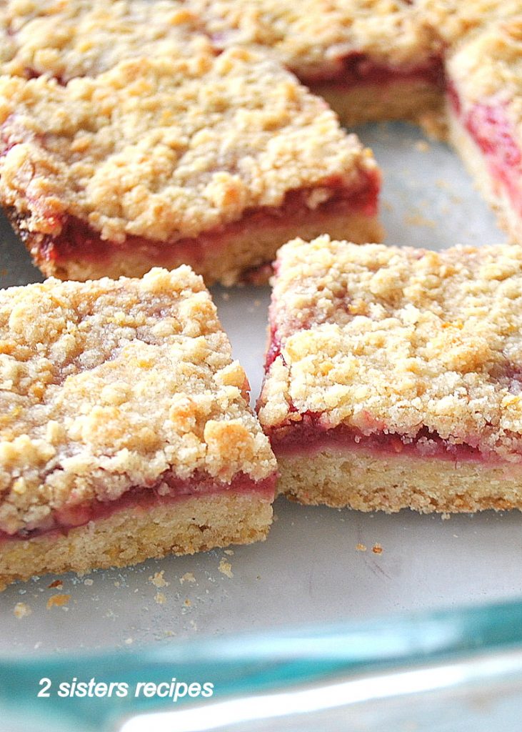  Raspberry bars are cut into squares inside its glass baking dish. 