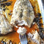 A large piece of red snapper roasted on a baking pan with juices and rosemary sprigs.