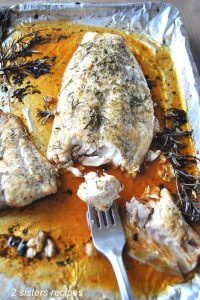A large piece of red snapper roasted on a baking pan with juices and rosemary sprigs.