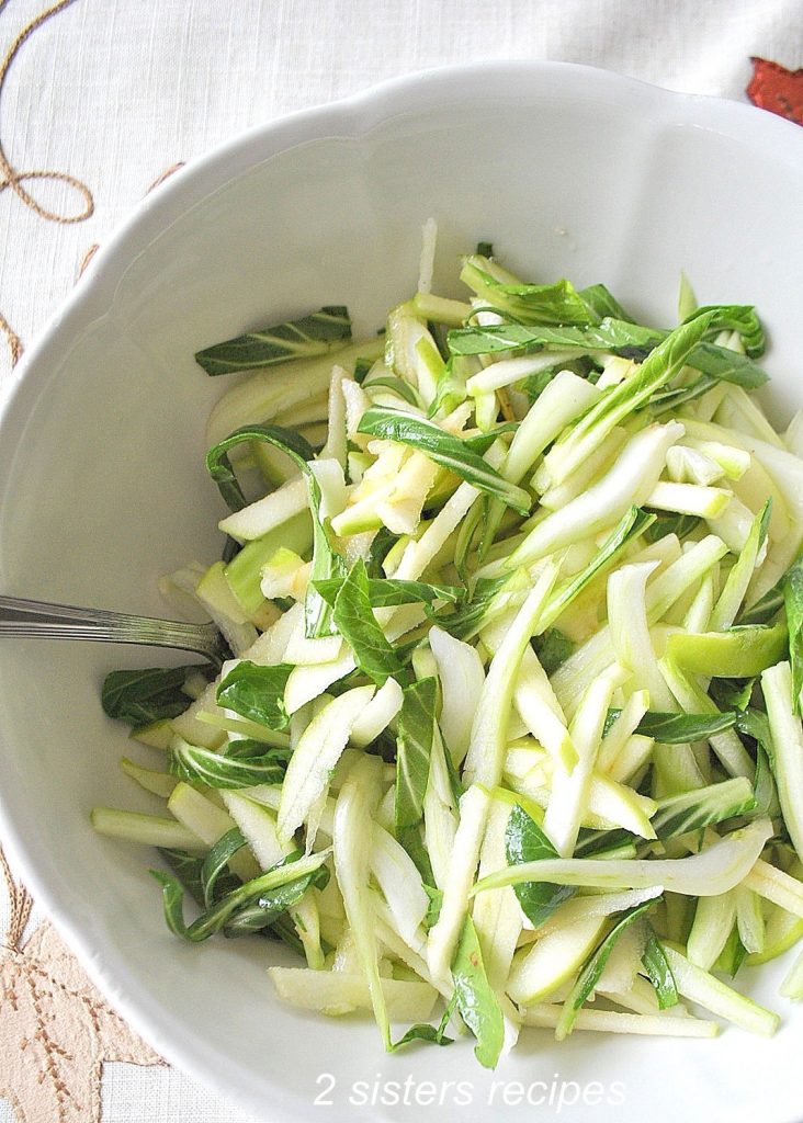 A white salad bowl with sliced green apples and sliced bok choy.