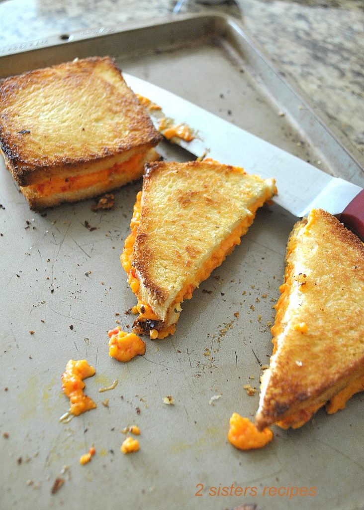 On a baking sheet, toasted cheese sandwiches are cut in halves. 